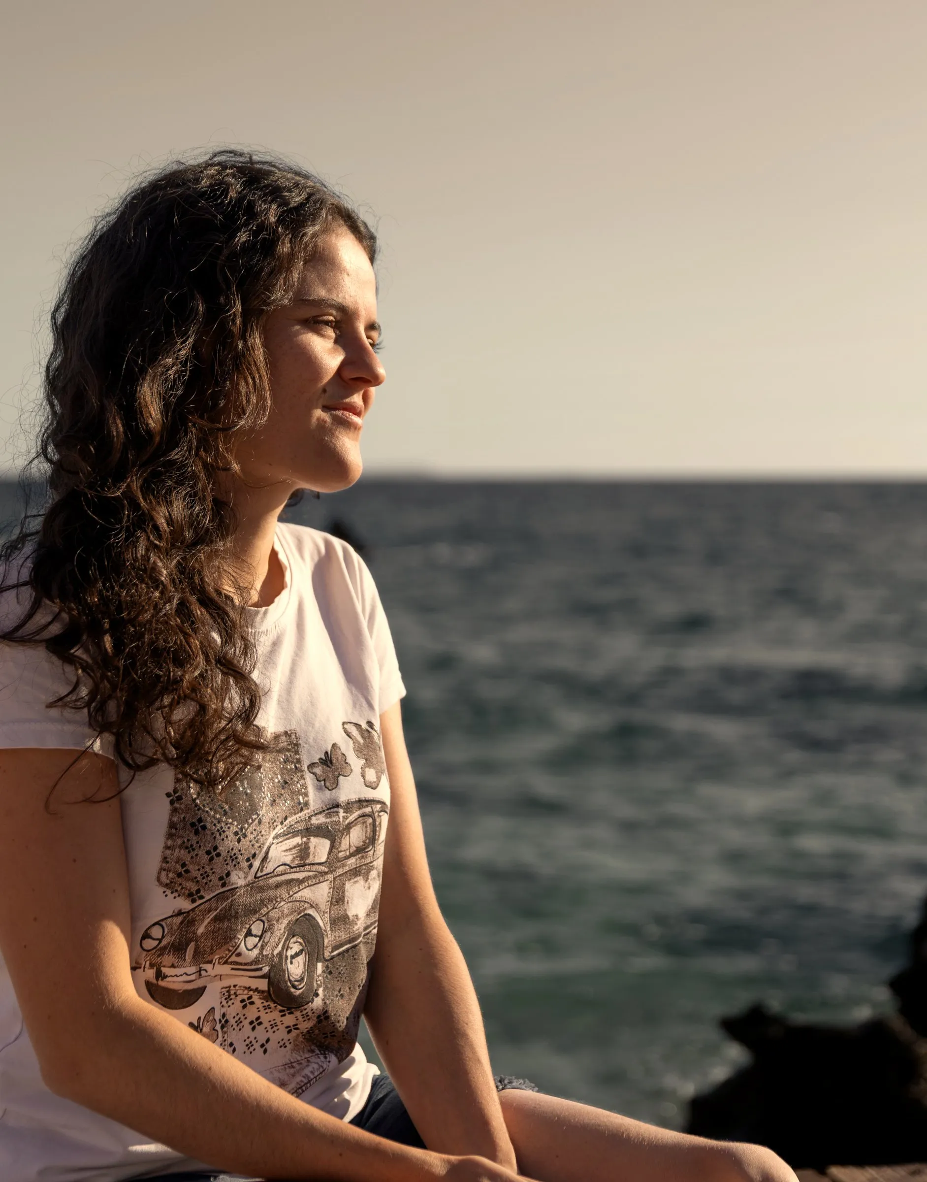 Grace sitzt am Meer und schaut in die Ferne